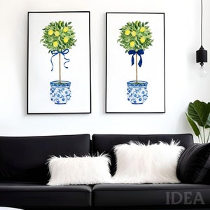 Pode incluir: Duas pinturas em aquarela emolduradas de &aacute;rvores de lim&atilde;o em vasos de cer&acirc;mica azul e branco com fitas azuis. As &aacute;rvores s&atilde;o de estilo topiary com formas redondas. As pinturas est&atilde;o penduradas em uma parede branca acima de um sof&aacute; preto.