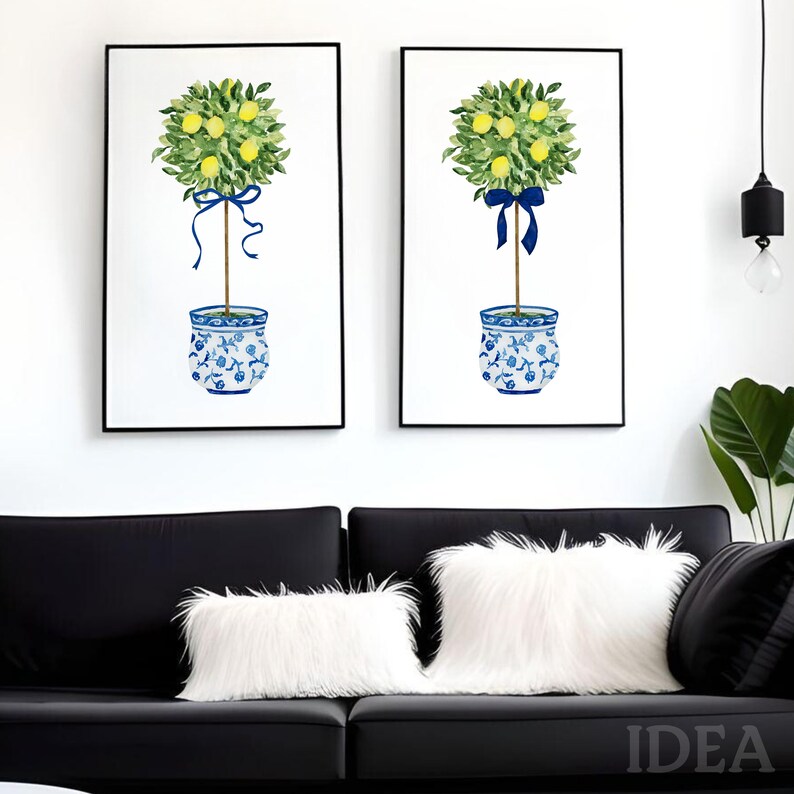 Pode incluir: Duas pinturas em aquarela emolduradas de &aacute;rvores de lim&atilde;o em vasos de cer&acirc;mica azul e branco com fitas azuis. As &aacute;rvores s&atilde;o de estilo topiary com formas redondas. As pinturas est&atilde;o penduradas em uma parede branca acima de um sof&aacute; preto.