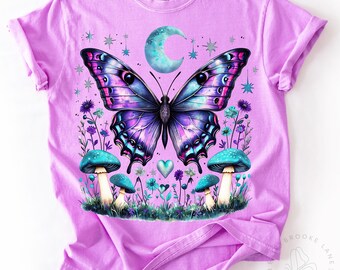 May include: A purple and blue butterfly with iridescent wings is surrounded by mushrooms and flowers on a lavender t-shirt. The butterfly has a crescent moon behind it.
