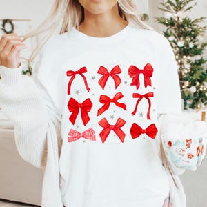 Puede incluir: Camiseta blanca con un dise&ntilde;o de lazos rojos. Los lazos son de varios estilos y tama&ntilde;os.