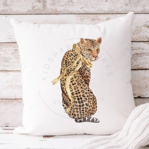 Puede incluir: Una almohada blanca con una ilustraci&oacute;n de acuarela de un leopardo con una cinta dorada. La almohada presenta el texto "Kidspace Designs" en un c&iacute;rculo.