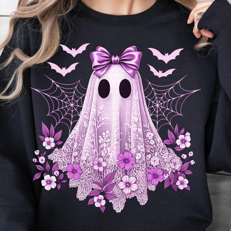 May include: Black sweatshirt featuring a lavender ghost design with a large bow, lace detailing, and floral accents. The design includes bats and spiderwebs, creating a spooky yet elegant Halloween theme.