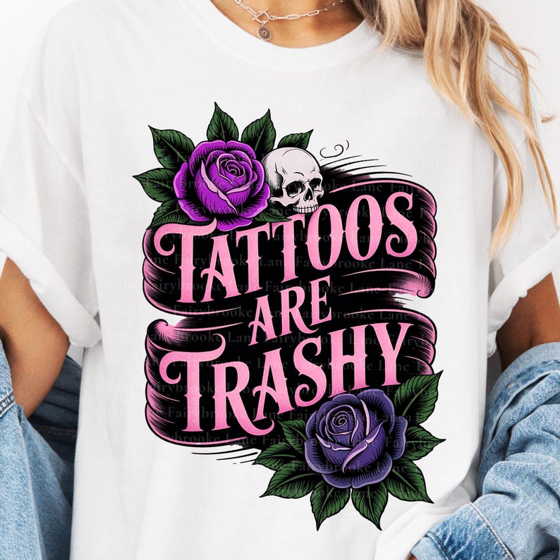 May include: White t-shirt featuring a graphic design with the text "Tattoos Are Trashy" in pink, adorned with purple roses, green leaves, and a skull. The design is centered on the shirt.