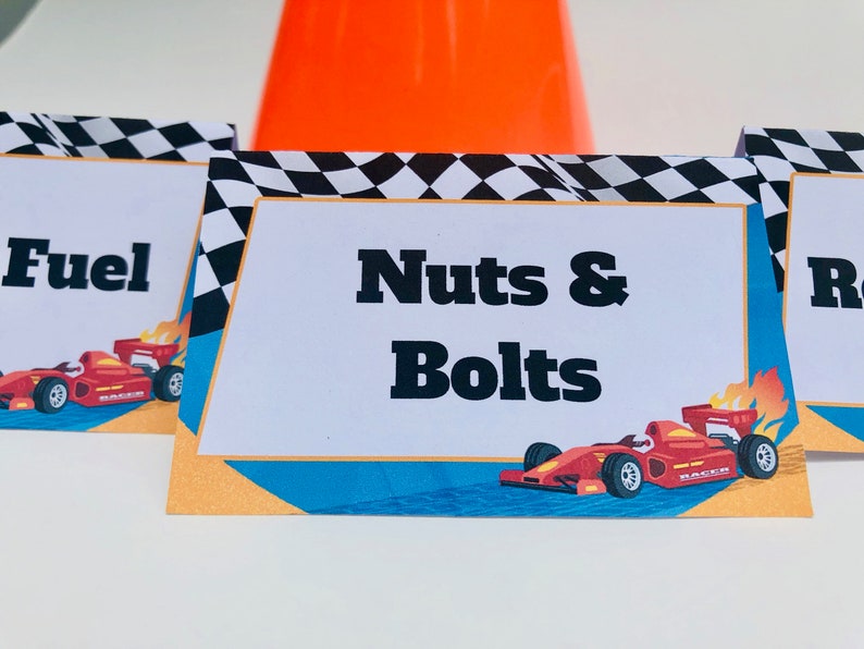Puede incluir: Tarjetas de mesa blancas con bordes a cuadros blancos y negros y un gr&aacute;fico de coche de carreras rojo. Las tarjetas tienen el texto "Fuel", "Nuts & Bolts" y "Racer". Un cono de tr&aacute;fico naranja est&aacute; en el fondo.