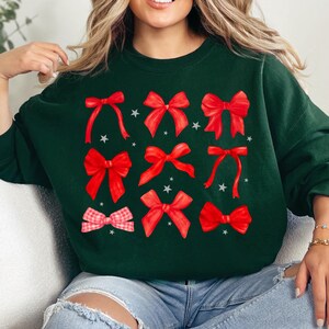 Puede incluir: Una sudadera verde oscuro con un dise&ntilde;o festivo que presenta m&uacute;ltiples lazos rojos de varios tama&ntilde;os y estilos. Los lazos est&aacute;n dispersos por la parte delantera de la sudadera.