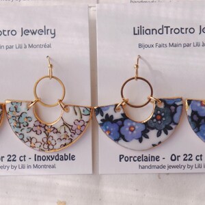 May include: Fan-shaped earrings with floral porcelain inserts and gold-coloured metal detailing. The earrings are marked with the text "LiliandTrotro Jewelry" and "Porcelaine - Or 22 ct - Inoxydable". The earrings are handmade in Montreal.