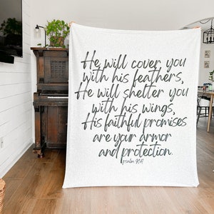 May include: White throw blanket with black text that reads "He will cover you with his feathers, He will shelter you with his wings, His faithful promises are your armor and protection. Psalm 91:4".