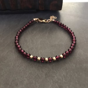 May include: A delicate bracelet made with small, dark red beads and gold accents. The bracelet is made with a simple design and is perfect for everyday wear.