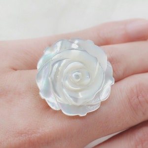 May include: A white mother of pearl ring featuring a rose design. The ring is made of natural shell and has a delicate, feminine look.