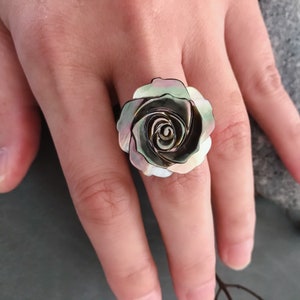 Peut inclure: Une bague ornée d'une grande rose irisée en nacre. La rose est de couleur vert foncé et noire avec des nuances de rose et de blanc.