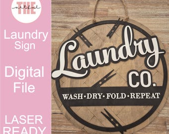 Może przedstawiać: Okrągły drewniany znak pralni z napisem "Laundry Co." w kolorze białym i czarnym. Znak zawiera frazę "Wash, Dry, Fold, Repeat" i dekoracyjne spinacze do prania. Do zawieszenia przymocowano linę.