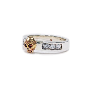 May include: A silver ring with a gold skull design and three small diamonds set in the band.