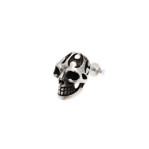 May include: A silver skull earring with intricate details and a black enamel finish.