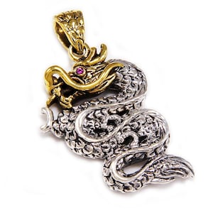 Puede incluir: Un colgante de dragón de plata y oro con un ojo de piedra preciosa rosa. El dragón está enroscado con la cola en la boca.
