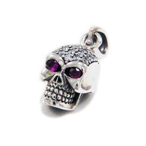Op de afbeelding: Zilveren schedel hanger met heldere en roze edelstenen. De schedel heeft een gedetailleerd ontwerp en is een populaire stijl van sieraden.