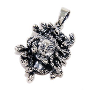 May include: A silver pendant featuring the face of Medusa, with snakes for hair. The pendant has a detailed, textured design and a loop for a chain. The Medusa pendant is a piece of jewelry.