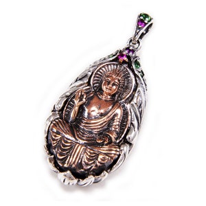 May include: A silver pendant with a detailed design featuring a copper-colored Buddha figure. The pendant is adorned with green and pink gemstones.