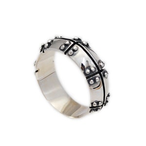May include: A silver ring with a textured design featuring a cross pattern and small dots around the edges.