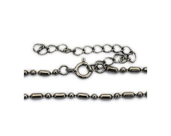 May include: A dark gunmetal gray chain necklace featuring a repeating pattern of small round beads and elongated cylindrical beads. The necklace includes a circular spring ring clasp and an adjustable extender chain with larger oval links.