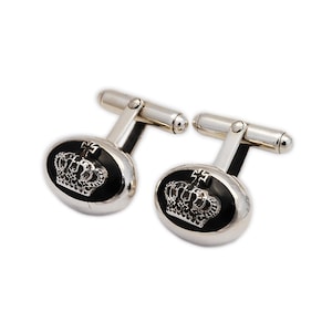 May include: A pair of silver cufflinks with a black enamel oval design featuring a silver crown with a cross on top.