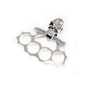 May include: Silver skull knuckle duster pendant featuring a detailed skull design. The skull has a menacing expression with sharp teeth and hollow eye sockets.