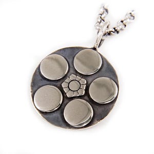 Puede incluir: Un collar con un colgante redondo de plata, adornado con cinco discos circulares y un diseño central en forma de estrella.