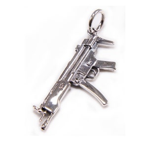 May include: A silver charm in the shape of a submachine gun. The charm has a loop at the top for attaching to a necklace or bracelet. The charm is marked "925" on the side, indicating that it is made of sterling silver.