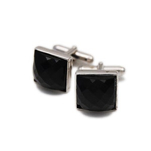 May include: A pair of square cufflinks with a faceted black stone set in a silver-tone metal frame. The cufflinks are displayed on a white background, showcasing their polished appearance and design.