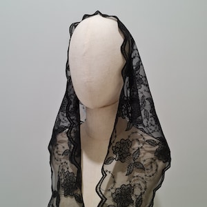 May include: Black lace mantilla with floral embroidery. The lace is delicate and sheer, with a scalloped edge. The mantilla is a traditional head covering worn by women in some cultures.