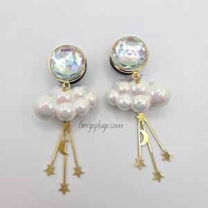 May include: A pair of iridescent crystal earrings with a cloud and star design. Each earring features a round crystal, a cluster of white pearl-like beads, and a dangling gold crescent moon with three gold stars.