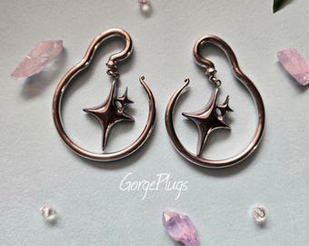 May include: A pair of silver hoop earrings with a dangling star charm. The star has a small crystal in the center.