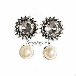 May include: A pair of silver earrings with a clear crystal center and a pearl drop. The earrings are in the shape of a sunburst.