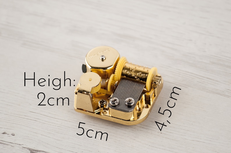 Puede incluir: Una caja de m&uacute;sica dorada con una llave de cuerda amarilla. La caja de m&uacute;sica mide 2 cm de alto, 5 cm de ancho y 4,5 cm de largo.