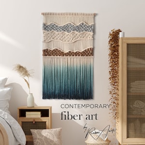 Könnte beinhalten: Ein zeitgenössischer Wandbehang aus Textilkunst in Blau-, Braun- und Weißtönen. Der Wandbehang ist aus Garn gefertigt und hat unten einen Fransen. Der Text "CONTEMPORARY fiber art by Riame Arts" ist unter dem Wandbehang sichtbar.