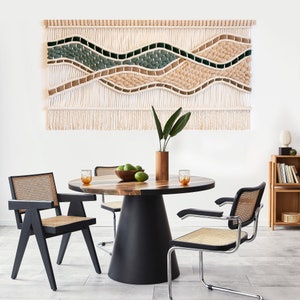 May include: A wooden dining table with a black pedestal base and a woven macrame wall hanging above it. The table is set with four chairs, two with black frames and woven seats and two with chrome frames and woven seats. There are glasses and fruit on the table.