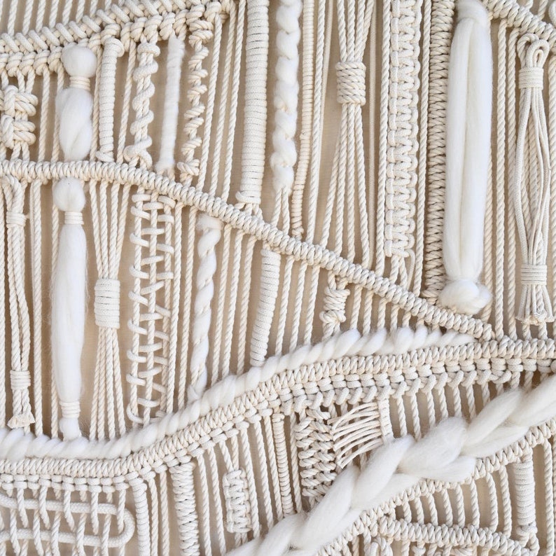 Puede incluir: Un tapiz de macram&eacute; blanco con una variedad de nudos y texturas. El tapiz est&aacute; hecho con cuerda de algod&oacute;n natural y presenta un dise&ntilde;o geom&eacute;trico &uacute;nico.