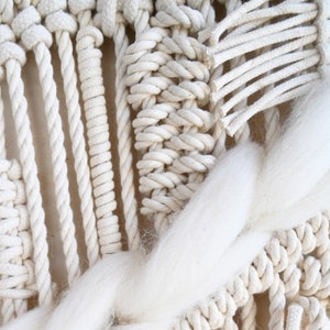 Puede incluir: Primer plano de un tapiz de macram&eacute; blanco con una fibra blanca esponjosa tejida en el dise&ntilde;o.