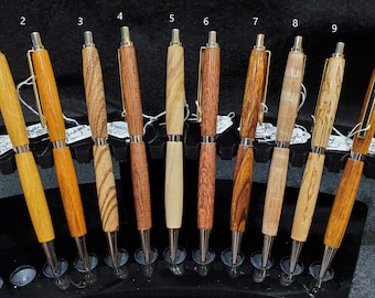 May include: Ten mechanical pencils with wooden barrels in various shades of brown, tan, and cream, each featuring a silver-toned metal clip, tip, and click mechanism. The pencils are numbered one through ten and displayed in a black stand.
