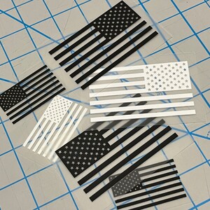 May include: Five different American flag decals, each with a different design. The flags are black and white, with the stars either black or white. The decals are on a clear background.