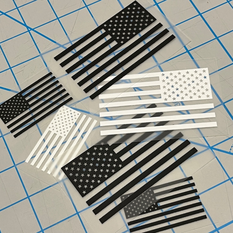 May include: Five different American flag decals, each with a different design. The flags are black and white, with the stars either black or white. The decals are on a clear background.