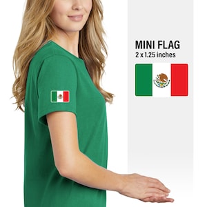 May include: A green t-shirt with a small Mexican flag patch on the left sleeve. The flag is 2 x 1.25 inches. MINI FLAG is written in black text above the flag.