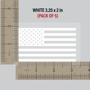 May include: A pack of five white 3.25 x 2 inch American flag decals. The decals are shown next to a ruler for size reference.