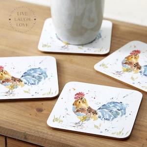 May include: A set of four square coasters with a watercolour rooster design. The coasters have a white background and a brown border. The rooster is depicted in blue, yellow, and red. A white mug sits on one coaster.