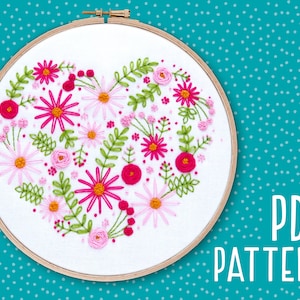 May include: Embroidered heart-shaped floral design in pink and green on white fabric in a wooden embroidery hoop.  PDF PATTERN text is visible below the hoop.
