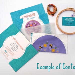 Contents of an embroidery kit including colourful threads, an embroidery hoop, a needle, a pre-printed fabric piece with a bee and flower design, felt padding, and an instruction booklet. Text at the bottom reads Example of Contents.