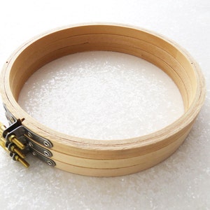 May include: A wooden embroidery hoop with a natural finish. The hoop is made of three layers of wood and has a metal tightening mechanism with three screws.