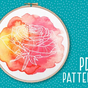 May include: A white outline of a rose is centered on a watercolor background of orange, yellow, and pink hues, set within a wooden embroidery hoop. The words "PDF PATTERN" are printed in white on a teal background.