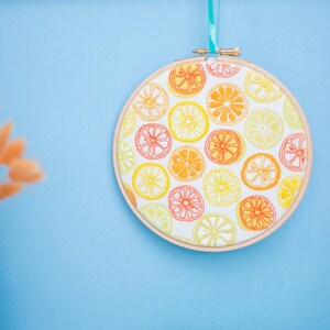 May include: A round embroidery hoop with a white fabric background and a pattern of orange and yellow lemon slices.