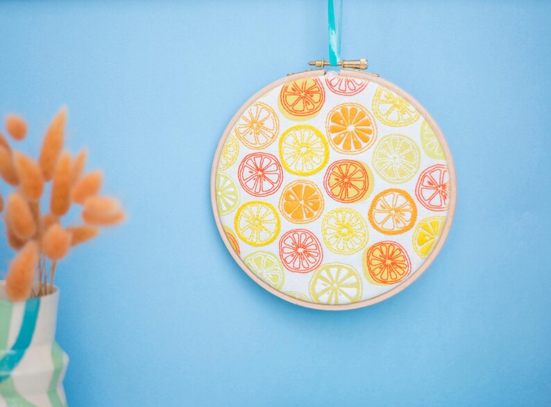 May include: A round embroidery hoop with a white fabric background and a pattern of orange and yellow lemon slices.