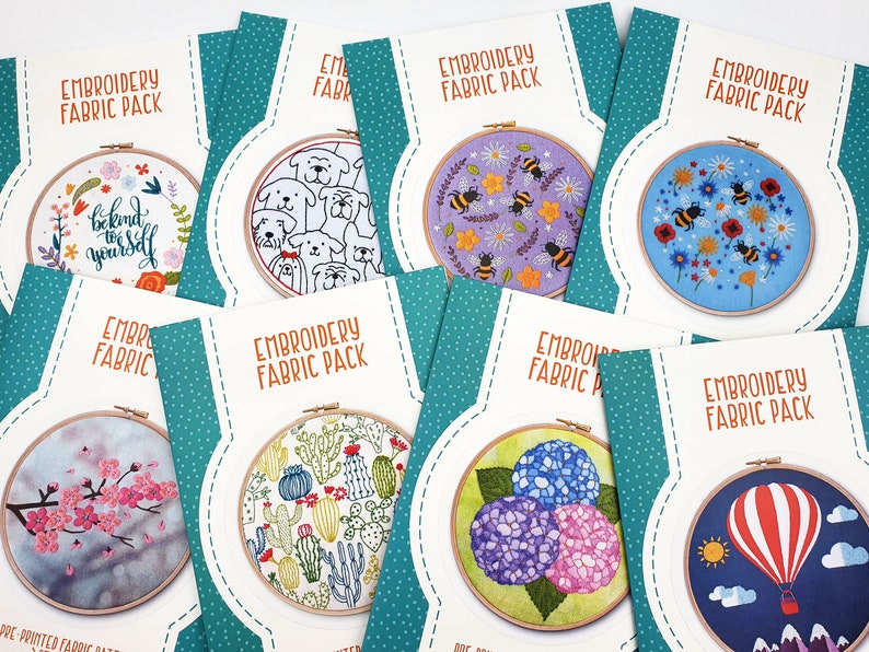 May include: Eight embroidery hoop kits with pre-printed fabric designs. The designs include a floral wreath with the text "be kind to yourself", a group of dogs, bees and flowers, bees and flowers on a blue background, a cherry blossom tree, a cactus garden, a cluster of hydrangeas, and a hot air balloon with mountains.
